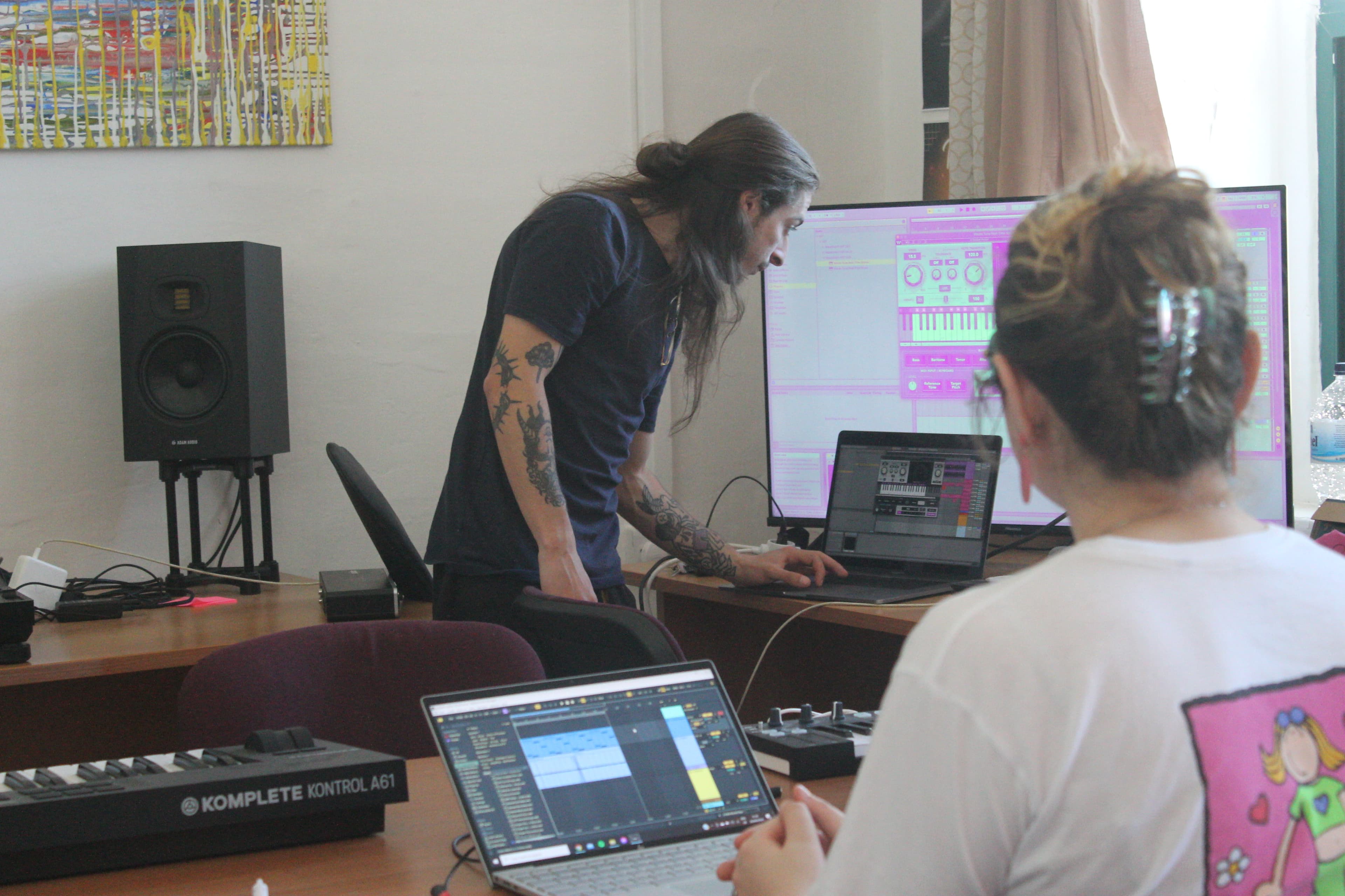 A production workshop at AISO Academy — the instructor demos a synth patch in Ableton Live on a large screen while students follow along at laptops