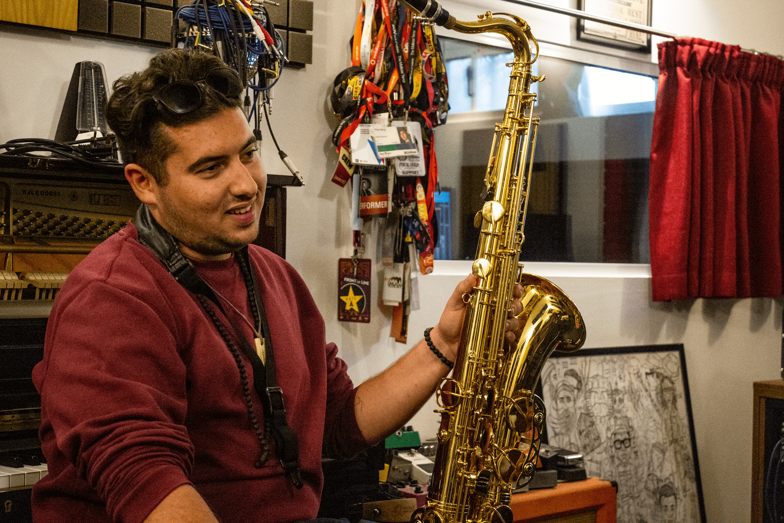A smiling musician holding a tenor saxophone in the academy's music room